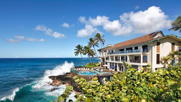 A beachfront hotel with a pool, palm trees, and ocean views.