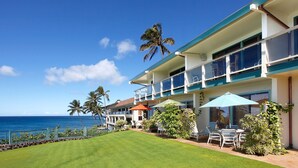 A beachfront hotel with a well-maintained lawn, outdoor seating, and a view of the ocean.