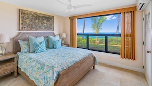 A bedroom with a large bed, a nightstand, a decorative wall piece, and a view of the ocean through a window.