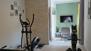 Une salle de sport à domicile équipée de matériel d’exercice, d’un téléviseur et d’un coin salon agrémenté d’une plante.