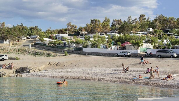 Une plage avec des gens, une étendue d’eau et des maisons en arrière-plan.
