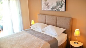 Un lit bien fait, recouvert d’une courtepointe matelassée, avec deux oreillers et une tête de lit. Une lampe de chevet se trouve sur le côté droit, et un tableau encadré est accroché au-dessus du lit.