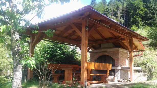 A rustic outdoor kitchen with a brick oven, wooden pergola, and a stone fireplace. - Holiday Home in Brod na Kupi by River Kupa (Delnice)