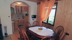 A dining room with a wooden table and chairs, a kitchen in the background, and a window with curtains. - Holiday Home in Brod na Kupi by River Kupa (Delnice)
