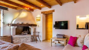 A cozy living room with a stone fireplace, wooden beams, a television, and a sofa. - Beautiful Villa Consisting of two Houses With Private Pool, Near Pula and Beach (Liznjan)