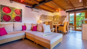A cozy living room with a sectional sofa, a dining table with chairs, and a stone wall. - Beautiful Villa Consisting of two Houses With Private Pool, Near Pula and Beach (Liznjan)