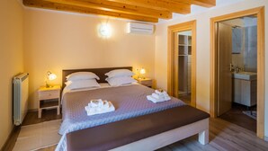 Een slaapkamer met houten plafond, een bed met witte lakens, twee bedlampen en een zichtbare badkamer door een geopende deur.