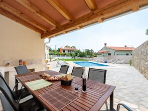 Un pati exterior amb una taula de fusta preparada per dinar, una piscina al fons i una paret de pedra.