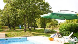 Una piscina con un ombrellone verde, lettini e un'area giochi sullo sfondo.
