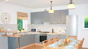 Una cucina moderna con mobili grigi, un forno a microonde, un fornello e un'area pranzo con sedie e tavolo in legno.