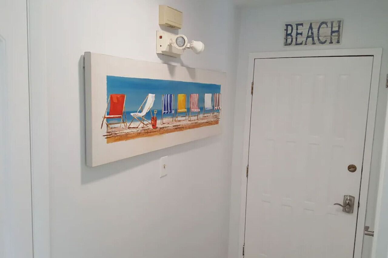 A room with a beach-themed painting on the wall, a door labeled "BEACH", and a ceiling-mounted air conditioning unit.
