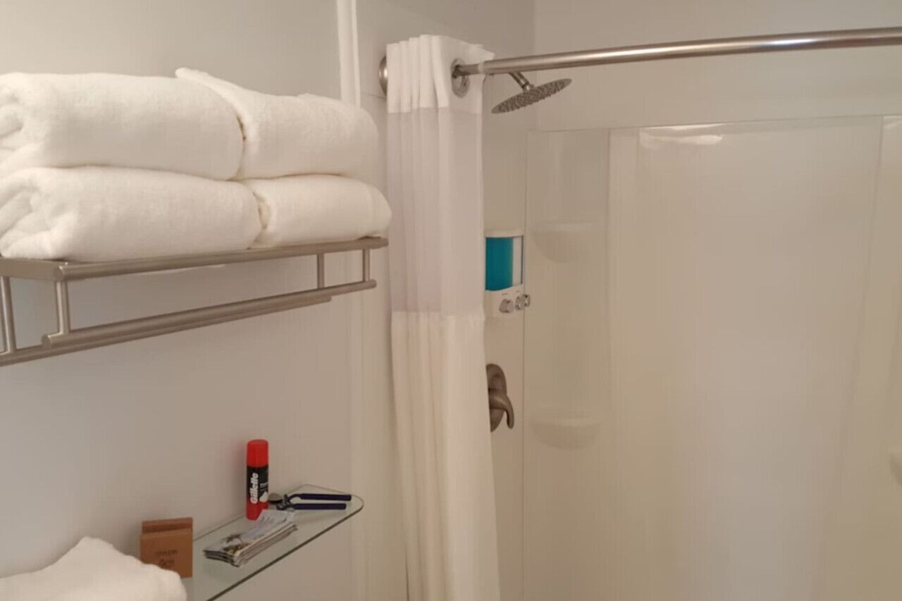 Un baño con cabina de ducha de vidrio, toallas blancas en un estante y artículos de aseo sobre una mesita.