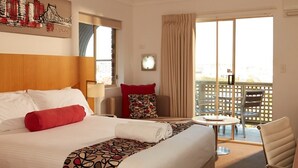 A hotel room with a large bed, a desk, a chair, a balcony, and a cityscape painting on the wall. - Private Room Brisbane (Spring Hill)