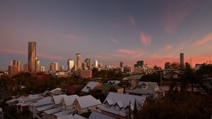 A cityscape with a mix of modern high-rise buildings and traditional houses under a sunset sky. - Private Room Brisbane (Spring Hill)
