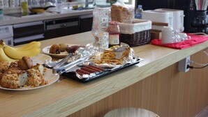 Una encimera de cocina con diversos alimentos, como plátanos, muffins y una bandeja de perritos calientes.