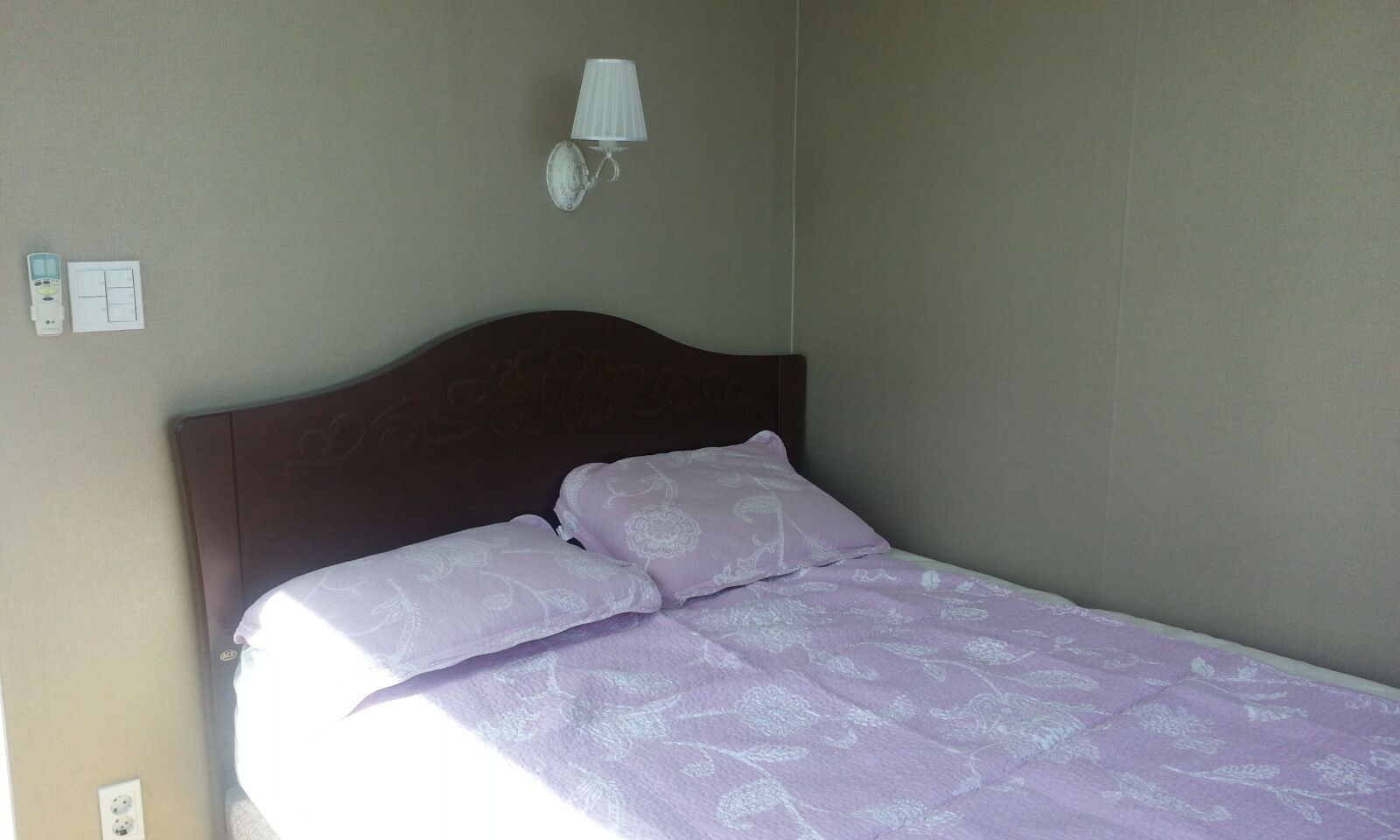 Uma cama de solteiro com cabeceira, uma luminária de cabeceira e uma tomada na parede.