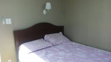 Uma cama de solteiro com cabeceira, uma luminária de cabeceira e uma tomada na parede.
