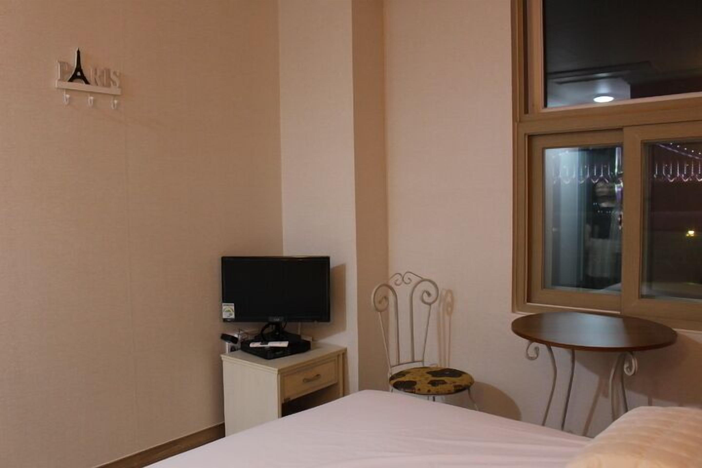 Habitación de hotel con cama, televisor sobre una mesita de noche, una pequeña mesa, una silla y una ventana.