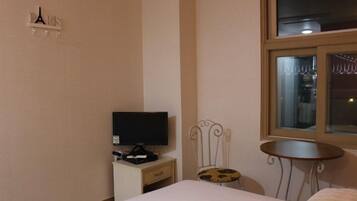 Habitación de hotel con cama, televisor sobre una mesita de noche, una pequeña mesa, una silla y una ventana.