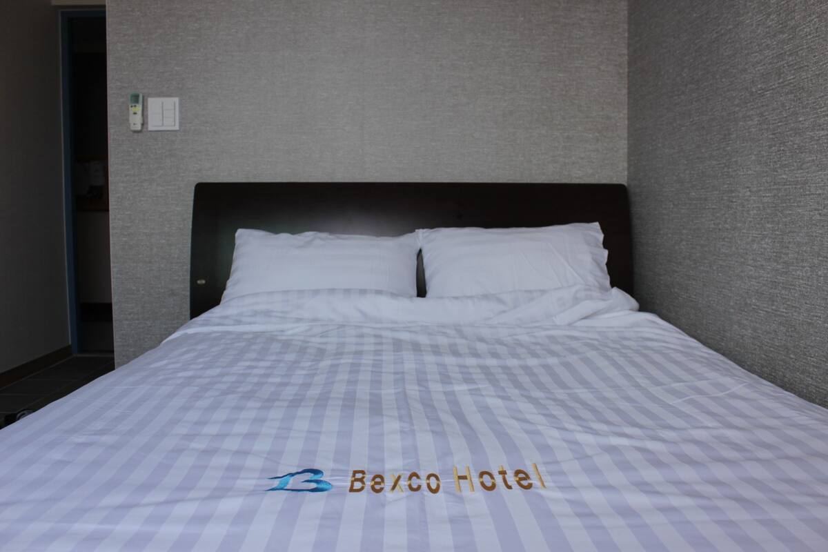 Une chambre d’hôtel avec un lit, une tête de lit et un interrupteur fixé au mur.