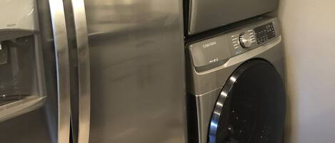 Een roestvrijstalen koelkast met een ingebouwd waterdispenser, en een verticaal geplaatst Samsung wasmachine en droger.