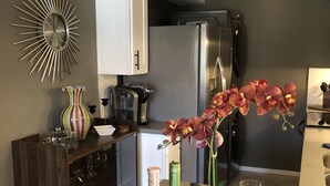 A modern kitchen with a central island, stainless steel appliances, and decorative elements like a sunburst mirror and orchids.