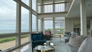 Un salon spacieux doté de grandes fenêtres, d’un ventilateur de plafond et offrant une vue sur la mer.