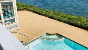 Une piscine avec vue sur la mer, entourée d’une zone sablonneuse et de verdure.