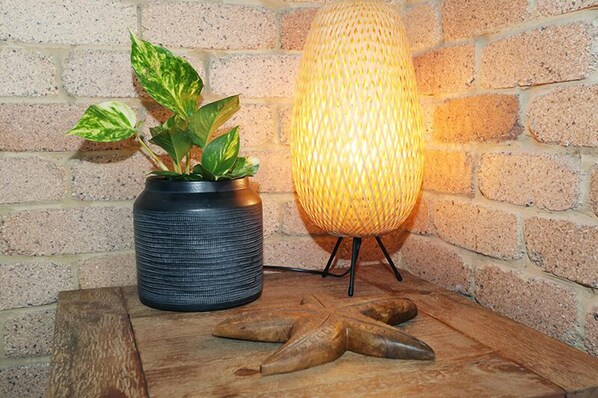 A potted plant with variegated leaves, a textured lamp on a stand, and wooden artifacts on a table against a brick wall.