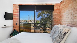 A hotel room with a large bed, a TV mounted on the wall, and a view of a marina through a glass door. - Illawong 7 (Mooloolaba)