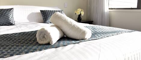 A neatly made bed with a patterned bedspread, pillows, and a rolled white towel.