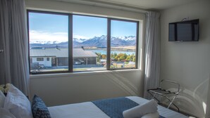 Une chambre d’hôtel dotée d’une grande fenêtre donnant sur les montagnes et un lac.