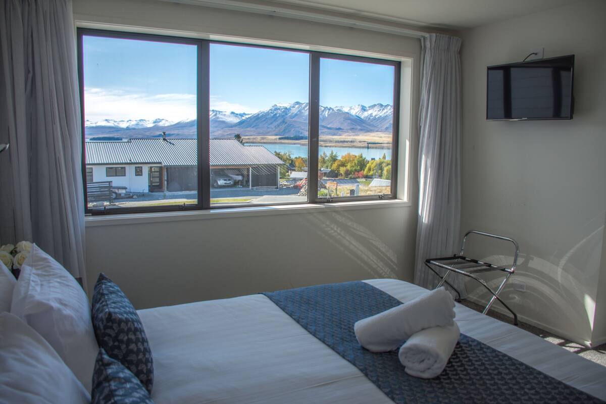 Habitación de hotel con un ventanal que ofrece vistas a montañas y un lago.