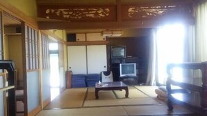 Un salón japonés tradicional con suelo de tatami, una mesa baja, un televisor y un sofá.