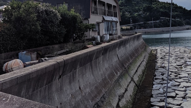 Un edificio costero con un muro de contención de concreto y un paseo adoquinado de piedra junto al agua.