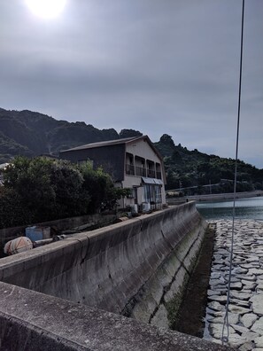 Un edificio costero con un muro de contención de concreto y un paseo adoquinado de piedra junto al agua.