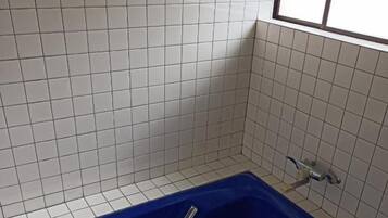 Une salle de bain avec une baignoire bleue, des murs recouverts de carreaux blancs et une fenêtre.