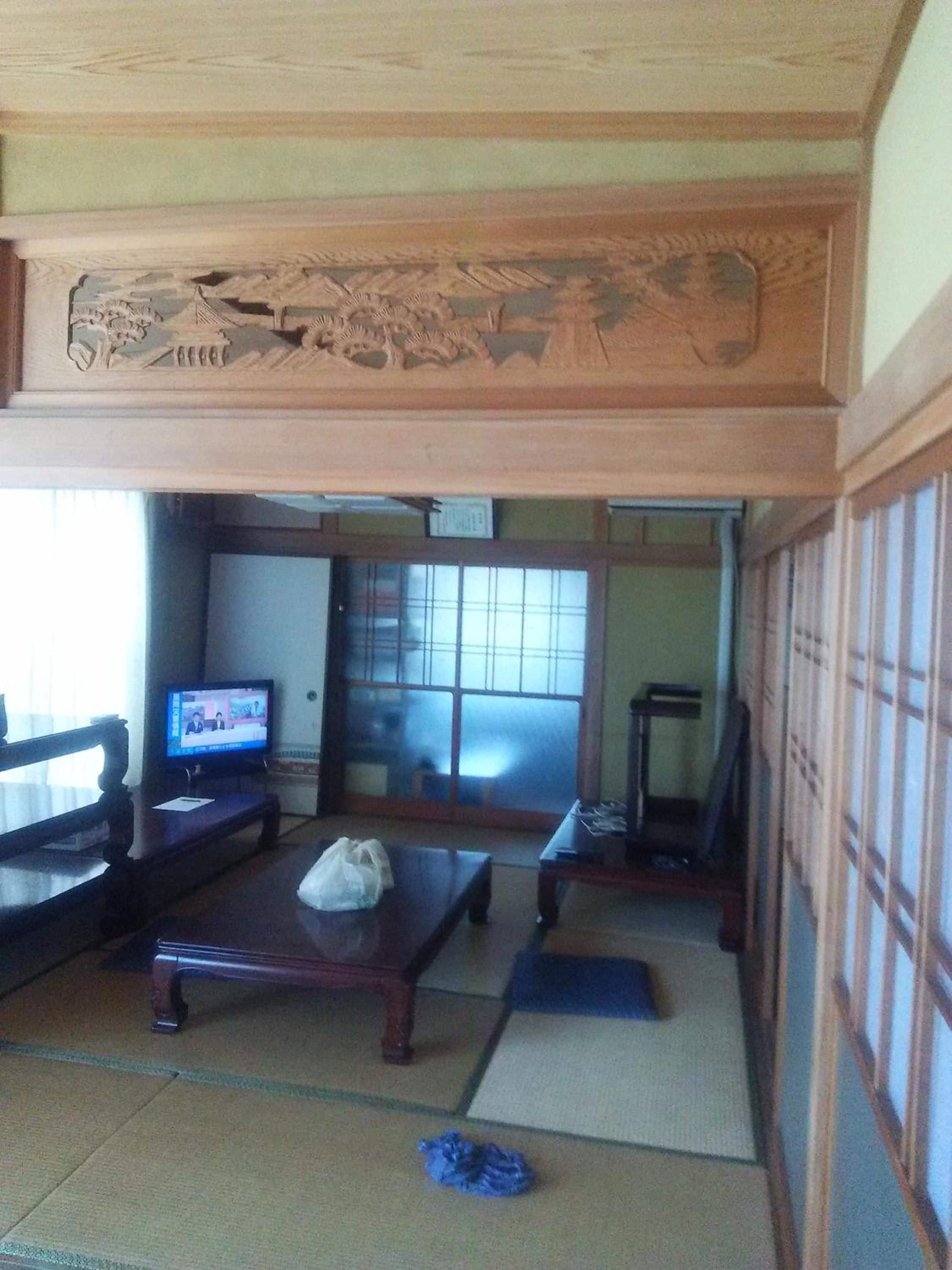 Una habitación japonesa tradicional con suelo de tatami, televisor, mesa de madera y puerta corredera.