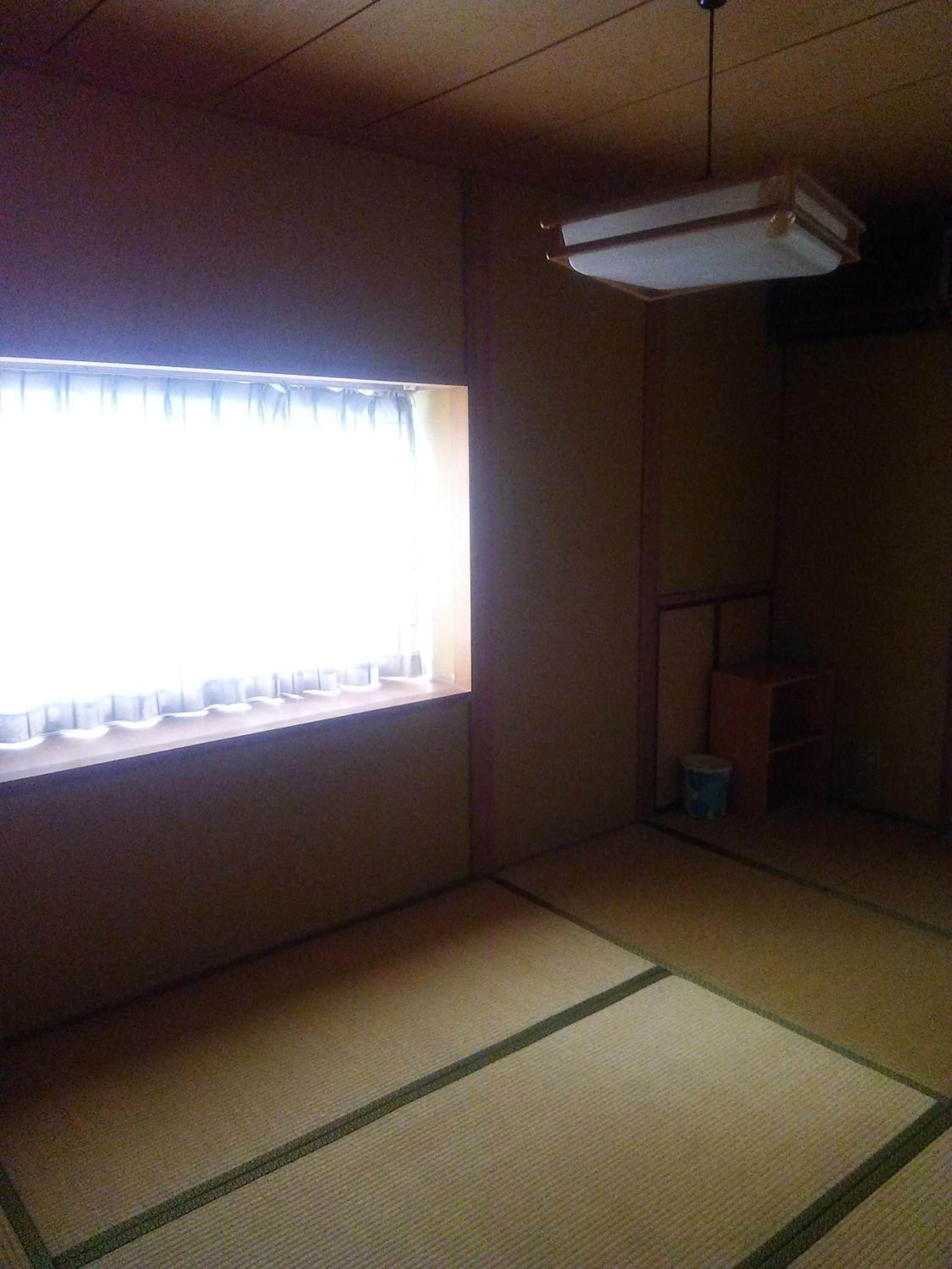 A room with tatami flooring, a window with curtains, and a ceiling fan.
