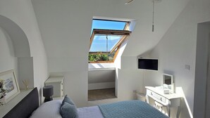 Une chambre avec un puits de lumière, un lit, un bureau et un ventilateur de plafond.