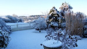 Un jardin enneigé, avec une clôture blanche, différents arbres et arbustes.