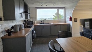 Une cuisine compacte dotée d’un îlot central, d’un coin repas avec une table et des chaises, et d’une grande fenêtre offrant une vue sur l’extérieur.