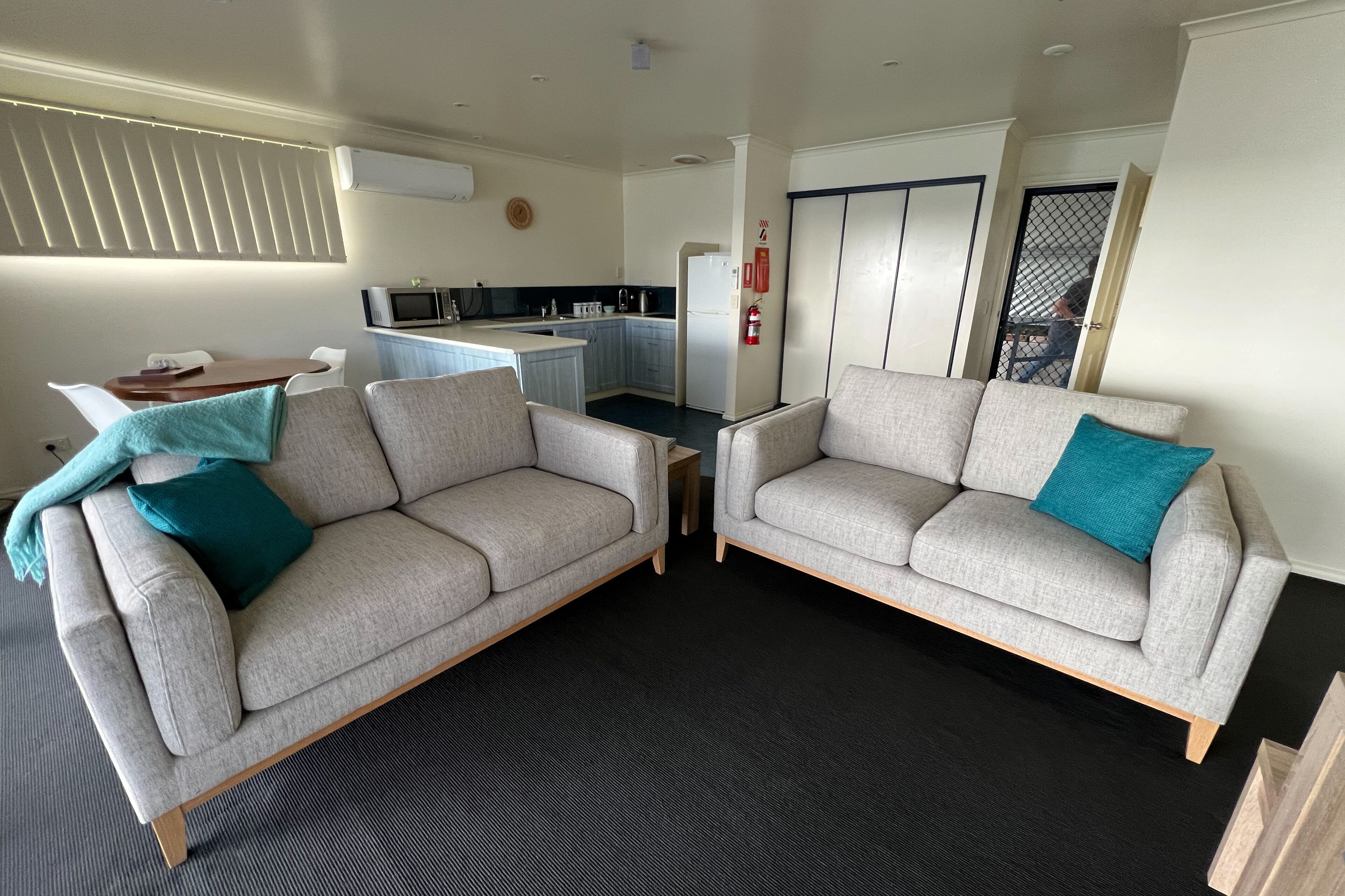 A living room with two grey sofas, a small table, and a kitchen in the background.
