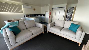 A living room with two grey sofas, a small table, and a kitchen in the background.