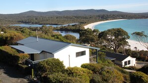 Ein modernes Haus mit Flachdach, umgeben von dichter Vegetation und mit Blick auf einen Strand und eine Bucht.