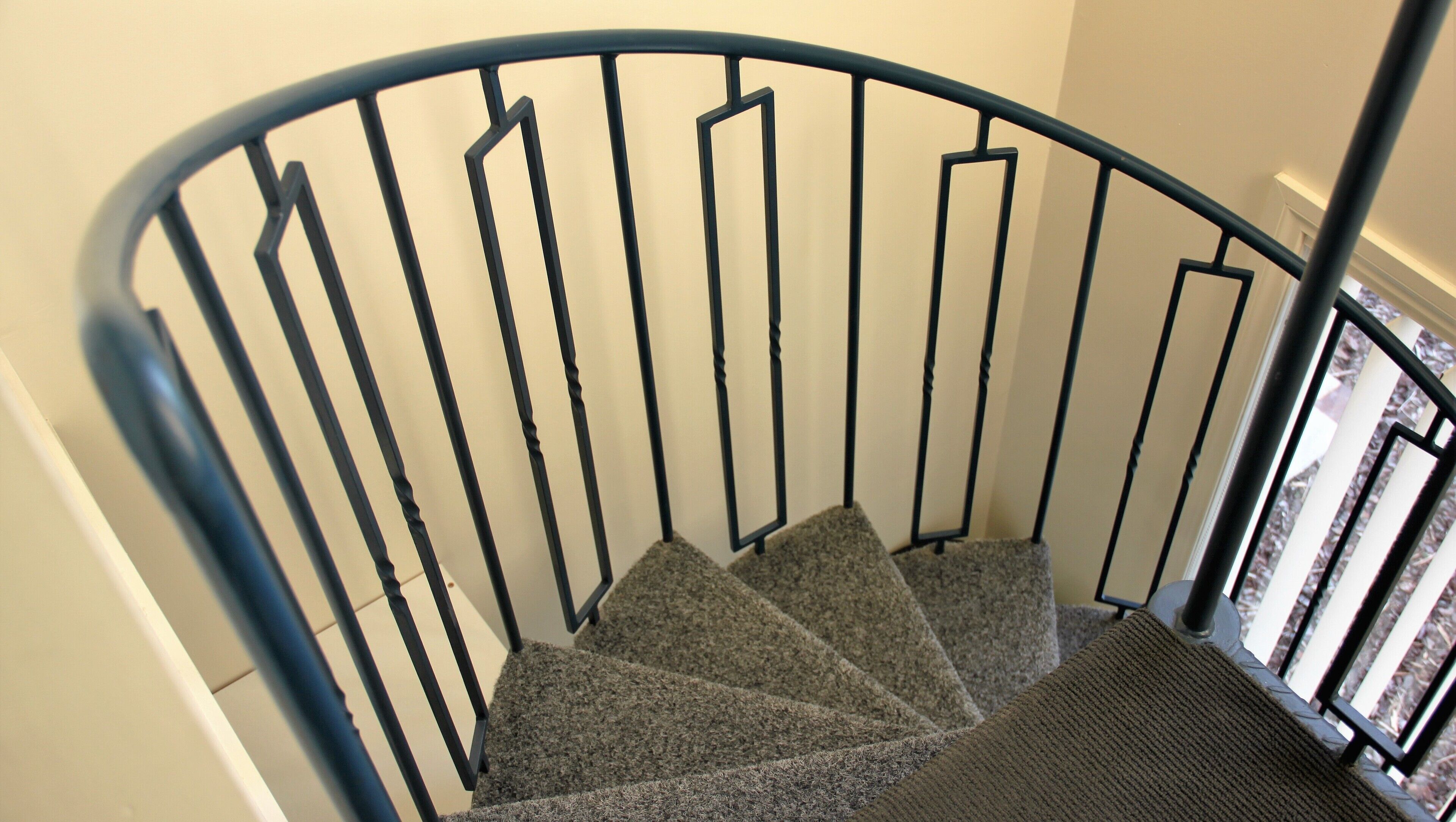 Un escalier en colimaçon avec une rampe en métal et des marches recouvertes de moquette.