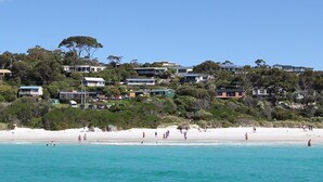 Eine Wohngegend an der Küste mit Häusern an einem Hang, einem Strand im Vordergrund und blauem Himmel.