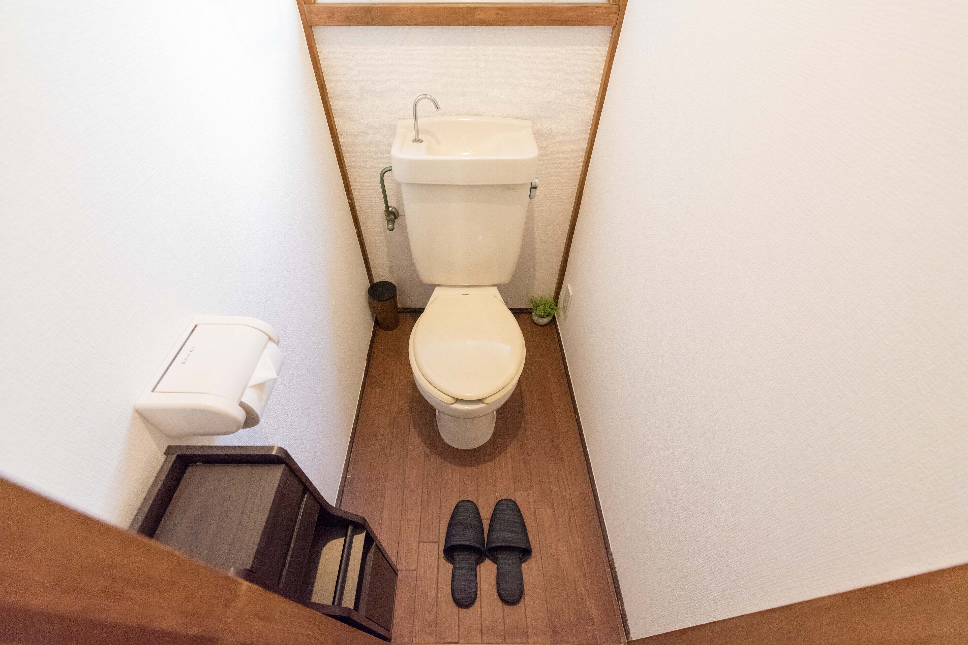 Une petite salle de bain avec des toilettes, un lavabo et une paire de pantoufles posées sur le sol.