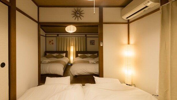 A hotel room with a large bed, two smaller beds, a ceiling fan, an air conditioning unit, and a traditional Japanese-style wall with shoji screens. - Yoshinaga Apartment 103 (Tokyo)