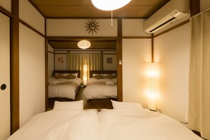Habitación de hotel con una cama grande, dos camas más pequeñas, un ventilador de techo, un equipo de aire acondicionado y una pared de estilo japonés con puertas correderas shoji.